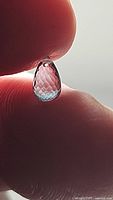 Close-up photo of the faceted teardrop-shaped Swiss blue topaz gemstone held between fingers, highlighting the drilled hole at the top for jewellery attachment.