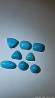 Nine polished natural turquoise cabochon gemstones arranged on neutral background showing variety of shapes and bright blue color