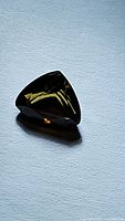 Photo of a 1.03 carat deep yellow cognac tourmaline gemstone with a trillion cut on a white surface, showing faceted reflections.