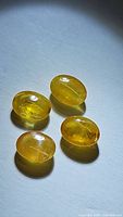 Four natural yellow sapphire oval cabochons placed on a white surface under natural light showing color, shape, and inclusions