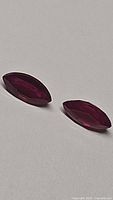 Pair of marquis cut blood red rubies on white surface showing deep color and clarity.