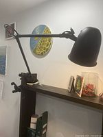 Black metal desk lamp mounted on a desk edge showing the adjustable arm and clamp base.