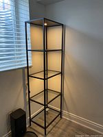 Full view of black metal and glass shelving unit with four shelves and top light illuminated