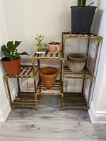 Photo showing the brown wooden corner plant shelf with five stepped slatted platforms, holding plant pots for scale.