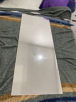 Top view of a large, rectangular frameless wall mirror laid flat on a bed with a grey blanket and colorful stripes.