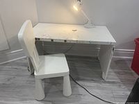 Wide view of white kids desk with chair and lamp, showing marks on desk surface, wooden construction, and chair positioned to side