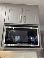 Front view of Magic Chef microwave installed in kitchen shelf showing the black and stainless steel body with digital display.