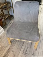 Front view of gray mesh chair seat and backrest with natural wood legs on light wood floor. Shows visible wear and surface marks.
