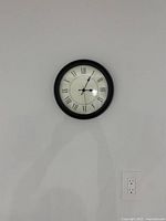 Front view of the NUFFRA wall clock mounted on a plain white wall showing the full face with Roman numerals and black frame.