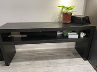 Full front view of the black wooden console table showing rectangular flat top and open shelf beneath with objects for scale and context.