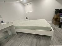 White queen size wooden bed frame with minor scuffs visible, shown assembled with a mattress placed on top.