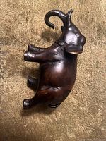 Side view of small brass elephant figurine showing trunk raised, large ears, tail, and legs.