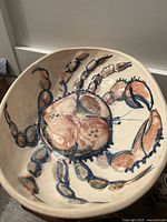 Top view of round ceramic bowl with detailed painted crab design in orange and blue on white background.