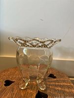 Clear crystal pedestal vase with scalloped rim and three feet on wooden surface