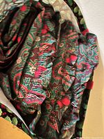 Close-up view of fabric pattern on cushions showing distinct red and green paisley and berry motif with ruched fabric and red pom-pom trim detail.