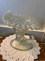 Photo of a clear glass boot shaped vase with hobnail texture, ruffled top edge, and curled toe on an oval base.