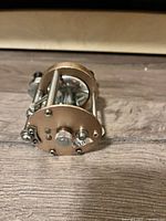 Close-up of front and side of vintage metal fishing reel with black wooden handles on crank.