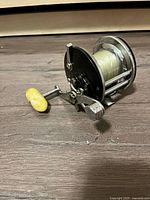 Side view of vintage fishing reel with spool of line and yellow handle grip on wooden surface