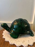 Side view of green ceramic turtle figurine on white textured mat, showing overall shape and shell details.