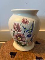 Front-side view of a cream-colored ceramic vase with hummingbird and flower relief decoration showing details of the paint and texture.