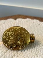 Top of lipstick case showing detailed floral engraving and signs of peeling on the gold tone finish.