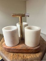 Front view showing three white marble cylindrical holders on a wooden base with a central T-shaped metal handle.