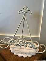 Metal decorative stand with intricate scroll and fleur-de-lis style design, paint chipping evident.