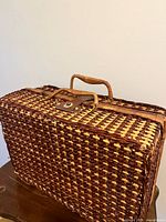 Side and top view showing woven wicker basket, leather latch with metallic twist-lock, and woven basket handle not properly attached.