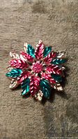Clear image of the pin showing the red, green, and gold metallic leaves in layered flower form with red rhinestones in the center.