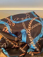 Nautical patterned scarf folded showing blue ropes and gold chains on black fabric.