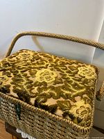 Photo of the top of a woven sewing basket with green and gold cushioned lid with floral pattern