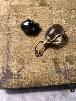 Two pendants on a textured fabric background, one small black skull pendant and one clear glass snake pendant.