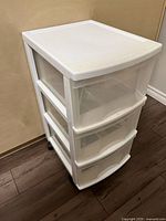 Front side view of white plastic storage drawers with three drawers and wheels.