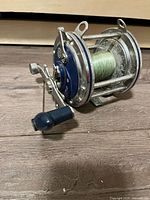 Fishing reel photographed from side angle showing handle and the blue and silver body with fishing line on spool.