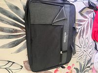 Front and side view of 100 Pipers black and gray fabric messenger bag laying flat on floral background