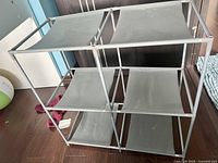View of the 3-tier gray storage organizer, showing the sturdy metal frame and fabric shelves from an angle where three shelves are visible.