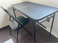 Side view of black metal folding table with folding chair beside it on dark wood floor.