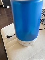 Front side view of the humidifier showing blue translucent tank, white base, buttons and power cable.