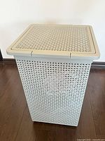 Photo of a large light gray plastic storage basket with an attached lid, showing woven style sides and a rectangular shape.