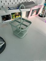 Photo of the mint-colored metal hanging organizer basket divided into four compartments on a white surface beside various desk items.
