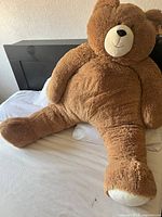 Large beige plush teddy bear sitting on a bed, showing its full front side including head, arms, legs, and belly.