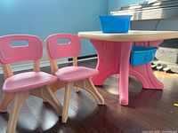 Photo of two pink and beige children's chairs and one round pink and beige children's table with blue storage bins attached.
