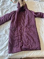 Purple synthetic winter coat with faux fur hood, zipper and snap button closure, size L, laid flat on bed.