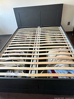 Full view of black queen bed frame with wooden slats and underbed storage construction.
