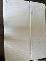 Photo of a white queen size foam mattress laid flat on a wooden floor, showing the surface texture and minor stains.