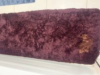 Close-up view of the burgundy shaggy carpet showing a noticeable large stain in one corner.