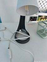 Gray and white table lamp with ribbed white lampshade and gray base, showing power cord with inline power switch and clear LED bulb.