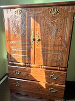 Front view of traditional walnut wood cabinet showing carved floral designs on doors, brass handles, and two drawers