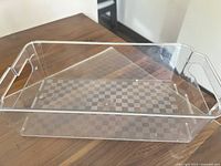 Clear rectangular polycarbonate tray with cutout handles on sides, placed on wooden table. Minor wear marks visible.