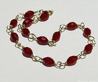 Bracelet laid out showing linked red beads and gold wire connections.